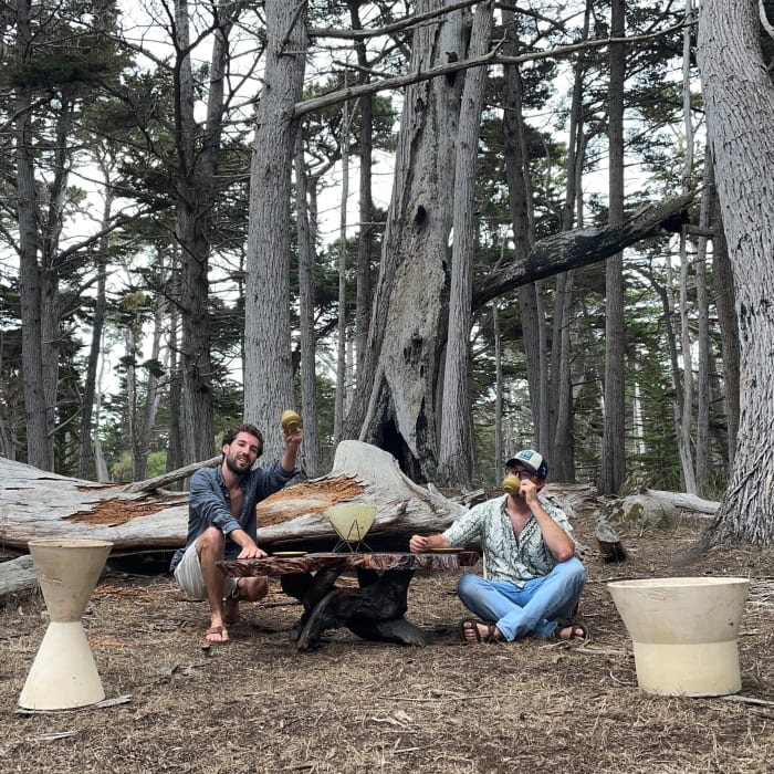 Chad and Bryce posing with a live-edge redwood coffee table and two Architectural Pottery planters  in a cypress forest outside of Monterey, California.